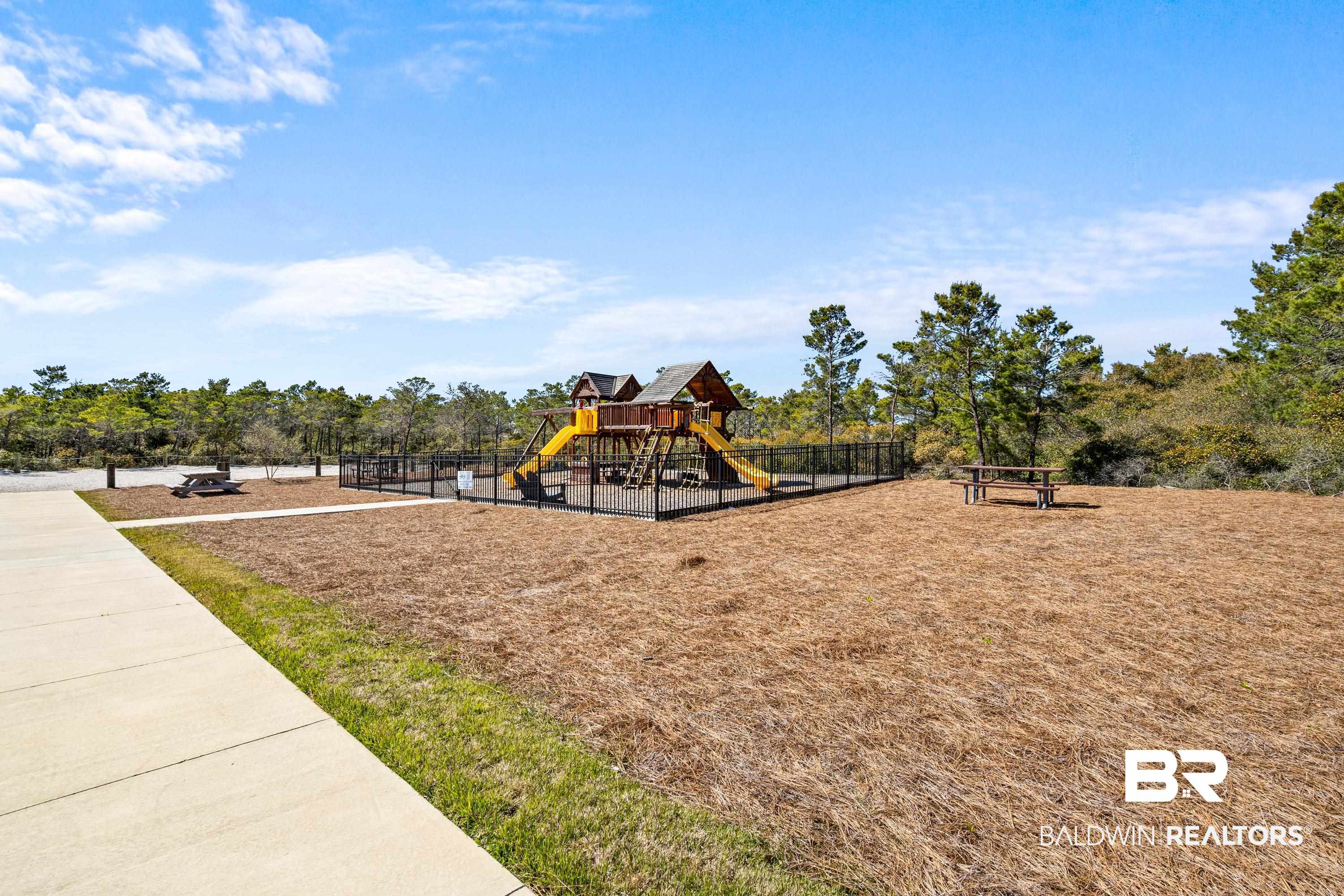 30194 River Road Orange Beach, AL 36561 - Photo 40 of 45 Outdoor recreation area featuring a fenced play structure with slides and a climbing wall, two picnic tables, and a concrete pathway