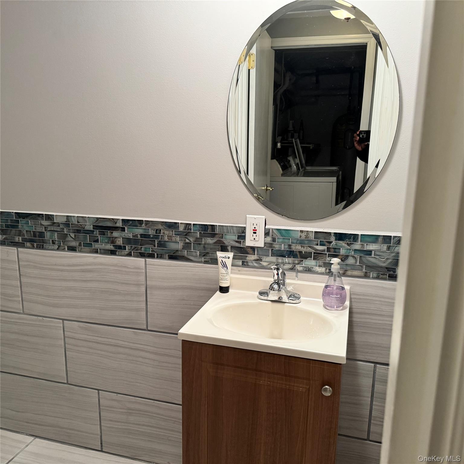 67 Steele Road New Windsor, NY 12553 - Photo 17 of 34 Vanity with integrated sink, wood-finish cabinetry, chrome faucet, beveled oval mirror, and decorative tile accent wall
