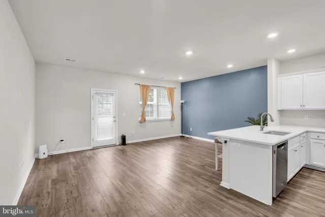 a kitchen with stainless steel appliances a stove top oven a sink dishwasher a refrigerator and white cabinets with wooden floor