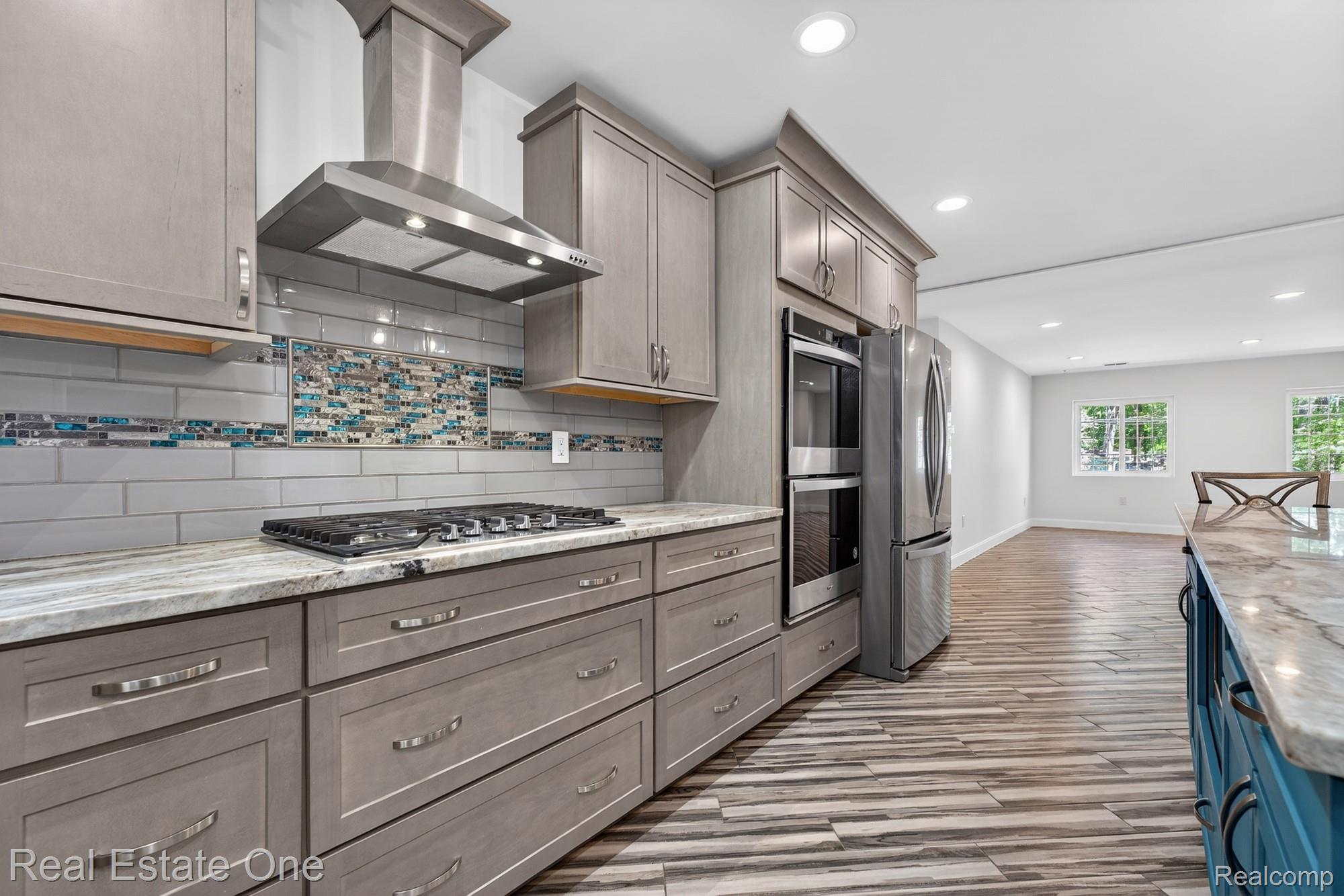26987 Crawford Road Romulus, MI 48174 - Photo 11 of 51 Modern kitchen featuring light gray cabinetry, stainless steel appliances, a gas cooktop, a stylish tile backsplash, and wood-finish flooring