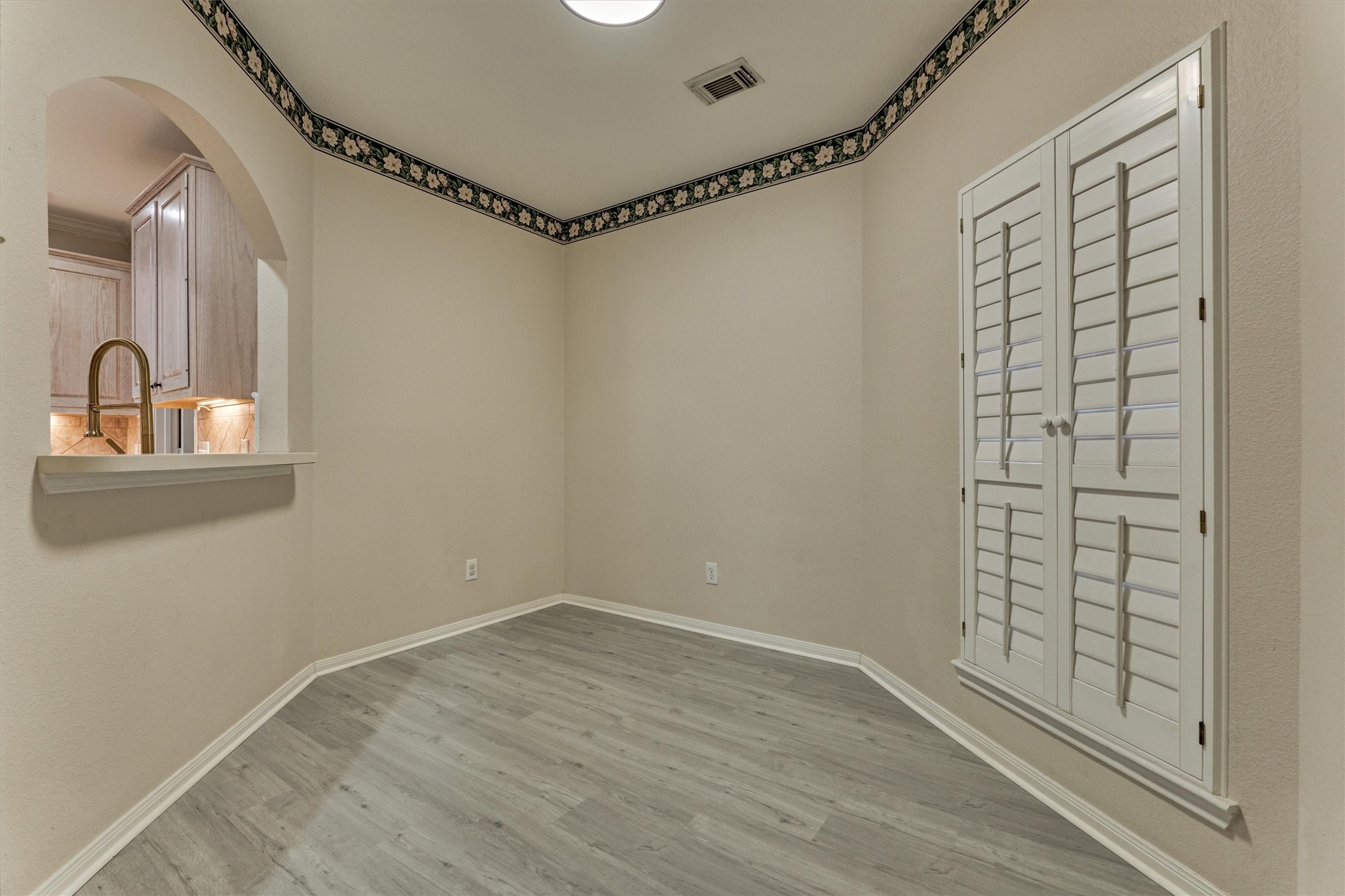 14420 Walters Road, Unit 26 Houston, TX 77014 - Photo 12 of 45 This room features light wood-look flooring, neutral walls, and a decorative border. It includes a window with white shutters and a passthrough to the kitchen. Perfect for a small dining area or office space.