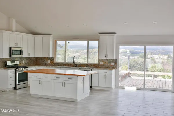 a large kitchen with granite countertop a stove a sink and white cabinets with wooden floor next to windows