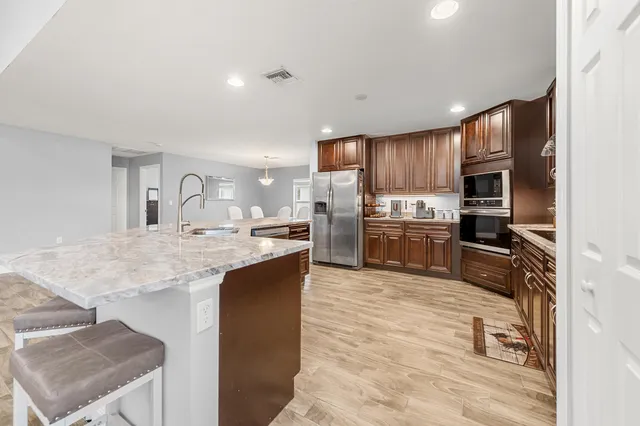 a kitchen with stainless steel appliances kitchen island granite countertop a refrigerator oven a sink dishwasher and white cabinets with wooden floor