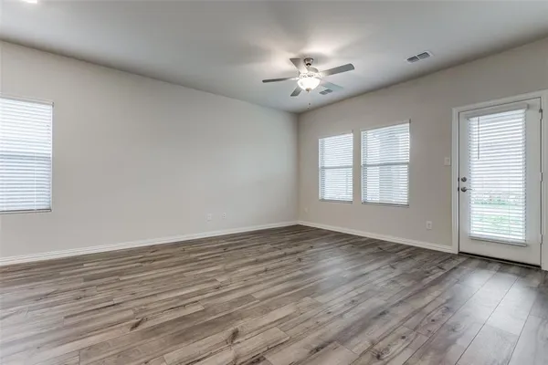 an empty room with wooden floor chandelier fan and windows