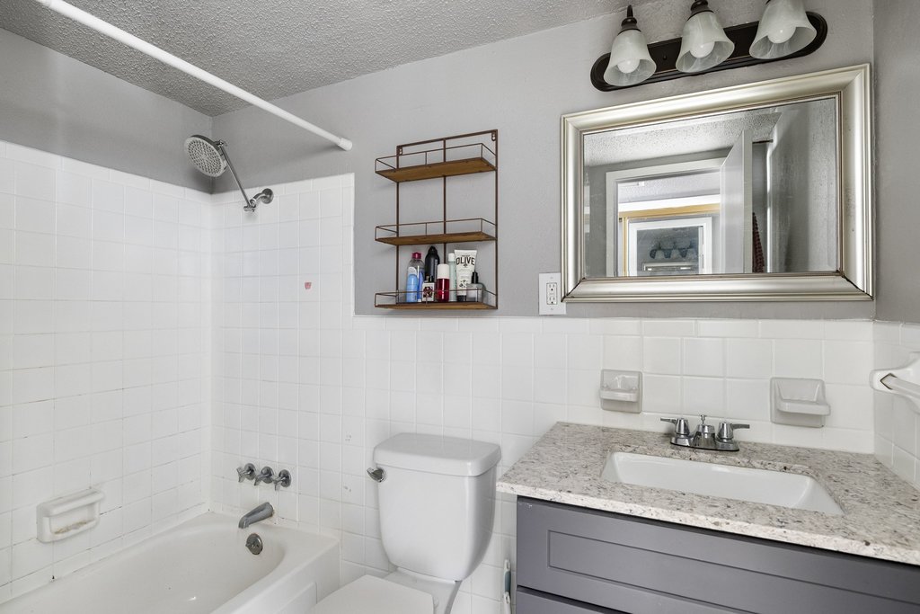 1800 Lavaca Street, Unit 207 Austin, TX 78701 - Photo 6 of 24 Bathroom with a textured ceiling, shower / bathtub combination, vanity, tile walls, and wainscoting
