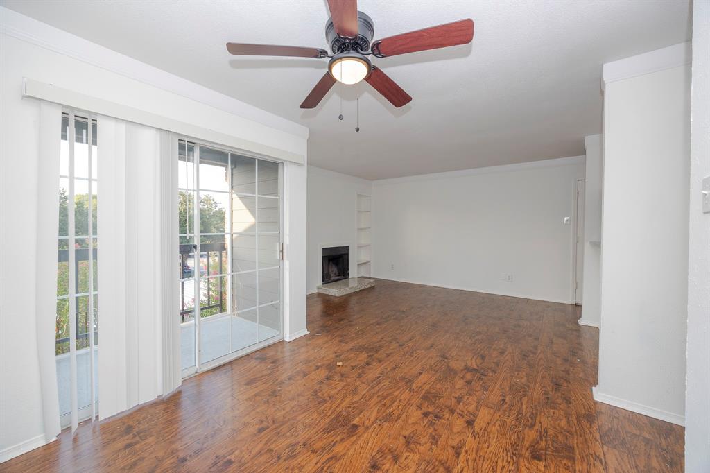 18333 Roehampton Drive, Unit 825 Dallas, TX 75252 - Photo 5 of 23 Spacious living area featuring wood-finish flooring, a ceiling fan with integrated lighting, and a fireplace with a hearth