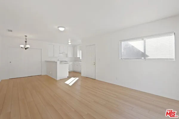 a view of an empty room with wooden floor and kitchen