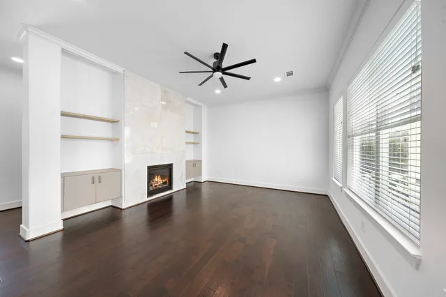 an empty room with wooden floor a ceiling fan a fireplace and windows