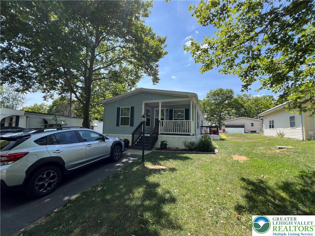 12 Springridge Road Bath, PA 18014 - Photo 3 of 61 Well-maintained manufactured home with a cozy front porch, nestled amidst mature shade trees.