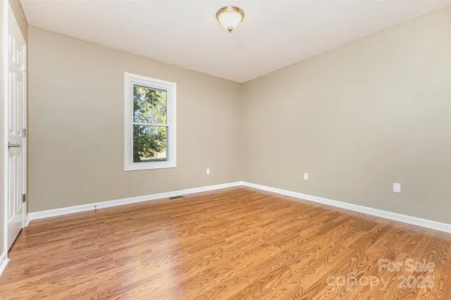 a view of an empty room with window and wooden floor