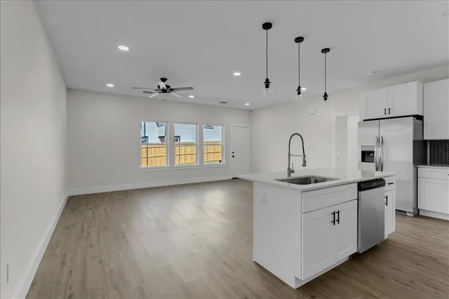 a kitchen with stainless steel appliances granite countertop a sink a stove a refrigerator and white cabinets with wooden floor