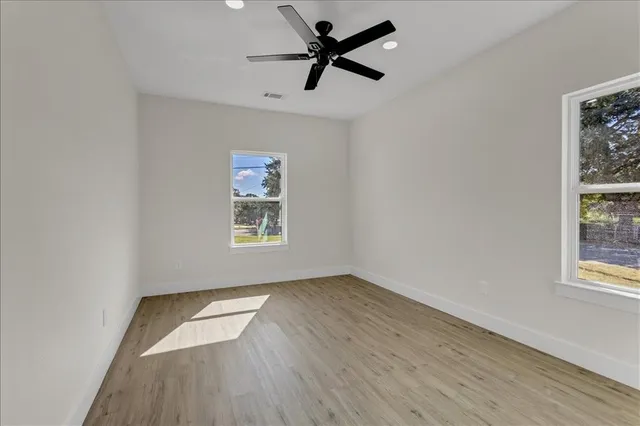 an empty room with wooden floor ceiling fan and windows