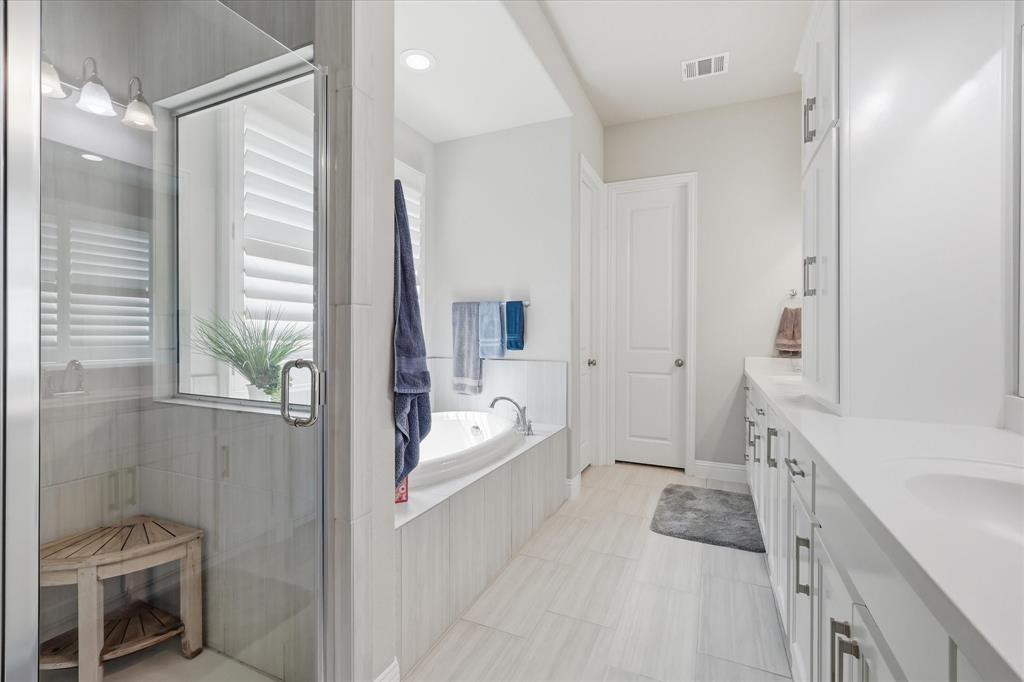 9708 Surveyor Road Oak Point, TX 75068 - Photo 22 of 34 Contemporary bathroom featuring a glass-enclosed shower with tile surround, a built-in soaking tub, dual vanities with integrated sinks, white cabinetry, and light wood-finish flooring