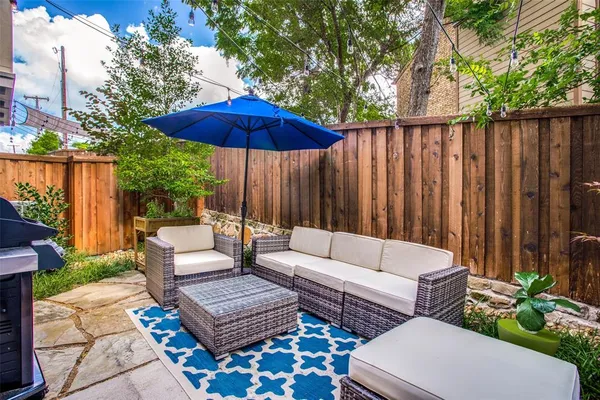 a view of a patio with couches table and chairs under an umbrella with wooden fence