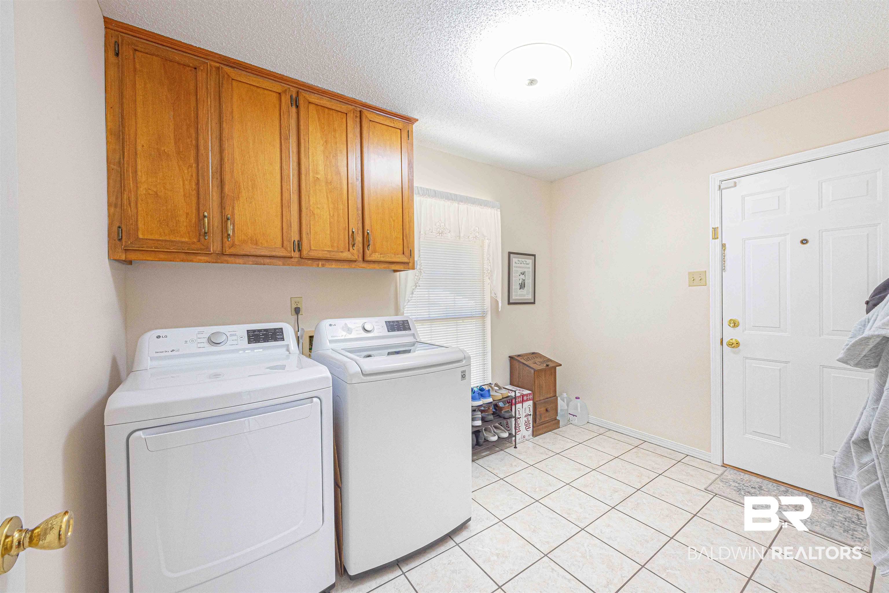 485 Ridgewood Drive Daphne, AL 36526 - Photo 34 of 38 Laundry area featuring washer and clothes dryer, a textured ceiling, light tile patterned flooring, baseboards, and cabinet space