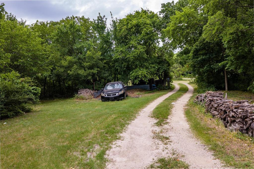 1007 West Belt Line Road Cedar Hill, TX 75104 - Photo 23 of 30 Gravel driveway with natural vegetation, bordered by a substantial stacked wood feature