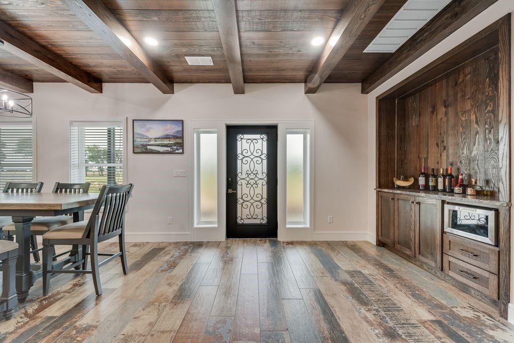 11167 Plainview Road Krum, TX 76249 - Photo 8 of 40 Entryway featuring a decorative wrought iron door, wood-finish flooring, exposed wood beam ceiling, and a built-in beverage bar with wood paneling and stone countertop