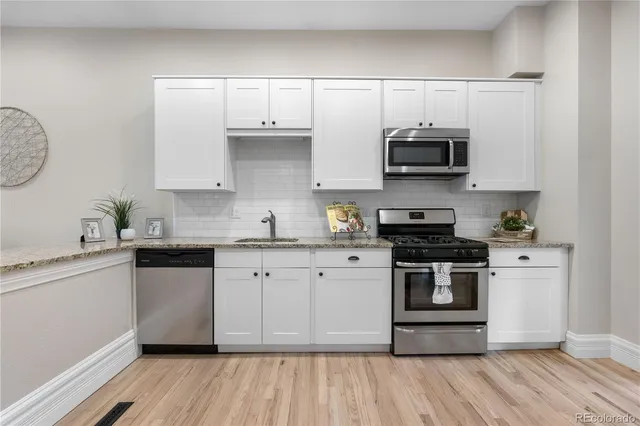 a kitchen with stainless steel appliances granite countertop a stove a sink and a white wooden cabinets