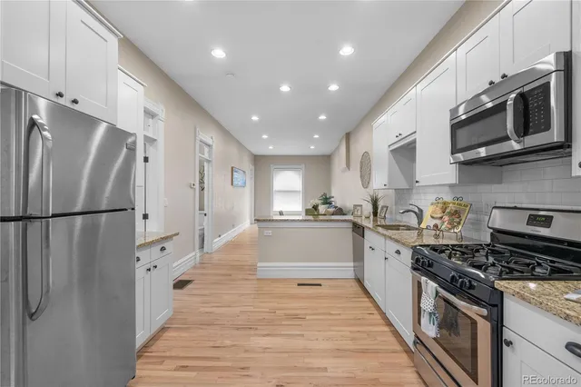 a large kitchen with stainless steel appliances granite countertop a large stove top oven a refrigerator white cabinets and wooden floor