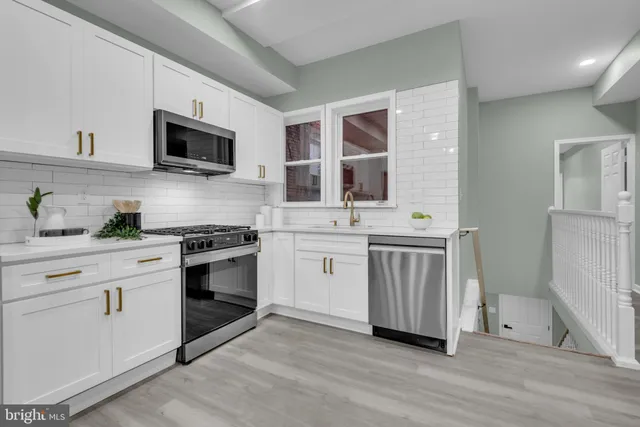 a kitchen with stainless steel appliances white cabinets a sink a stove a microwave and wooden floors