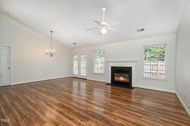 an empty room with wooden floor fireplace and windows