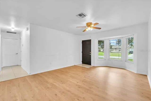 a view of an empty room with window and chandelier fan