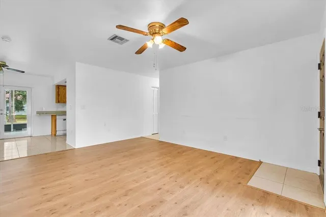 a view of an empty room with wooden floor and a ceiling fan