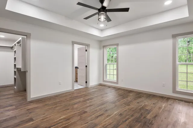 an empty room with wooden floor a ceiling fan and windows