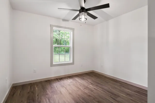 an empty room with wooden floor ceiling fan and windows