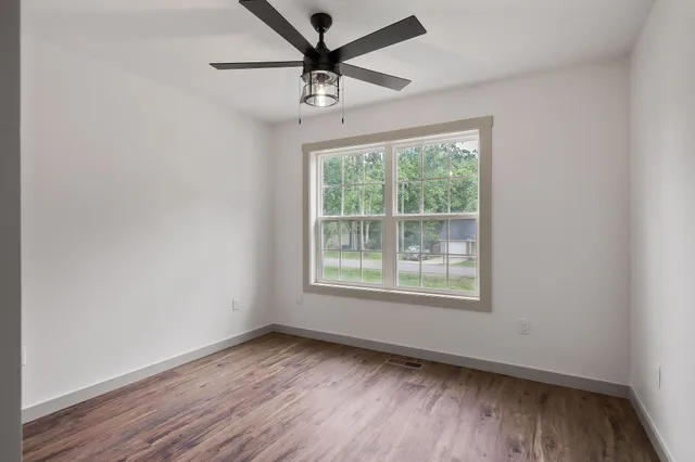 an empty room with wooden floor ceiling fan and windows