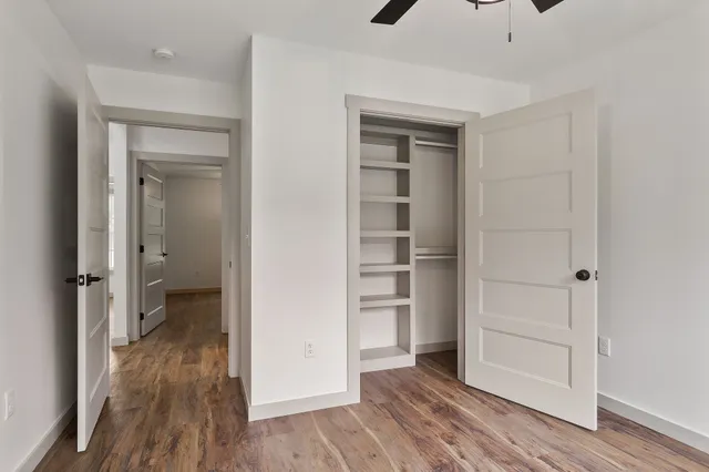 an empty room with wooden floor closet and windows