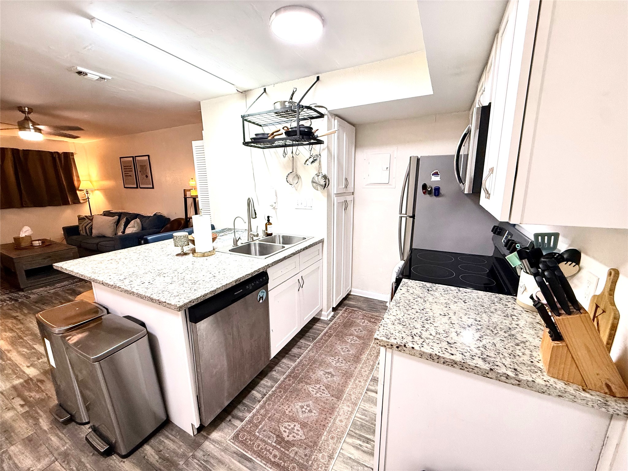 Kitchen featuring white cabinets, a peninsula, stainless steel appliances, light stone counters, and dark wood finished floors