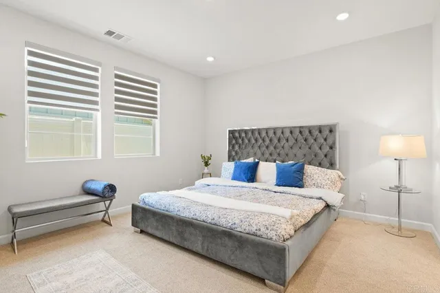 a spacious bedroom with a bed and a lamp on dresser