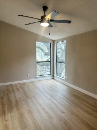 an empty room with wooden floor fan and windows