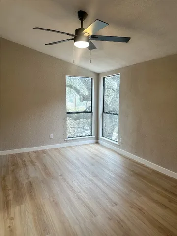 an empty room with wooden floor chandelier fan and windows
