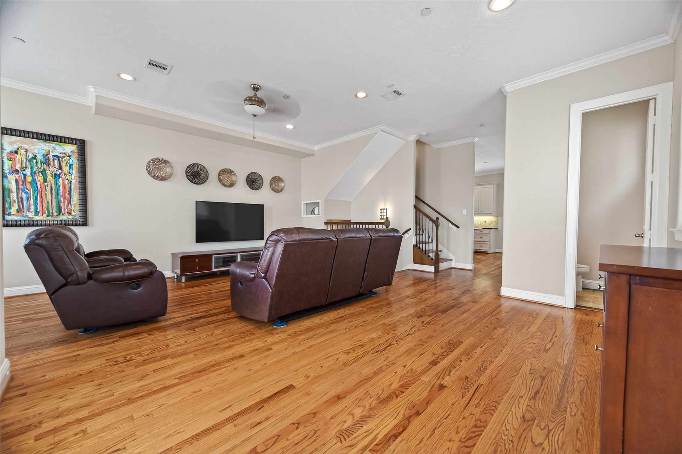 2611 Riverside Drive, Unit C Houston, TX 77004 - Photo 24 of 50 This spacious living room features hardwood floors, neutral walls, and recessed lighting. It includes comfortable leather seating, a wall-mounted TV, and decorative artwork, leading to a staircase and an adjacent open kitchen.