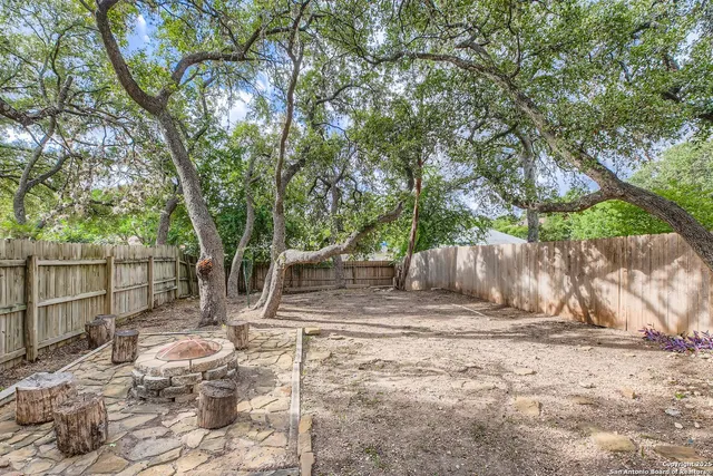 a view of a backyard with wooden fence and large trees