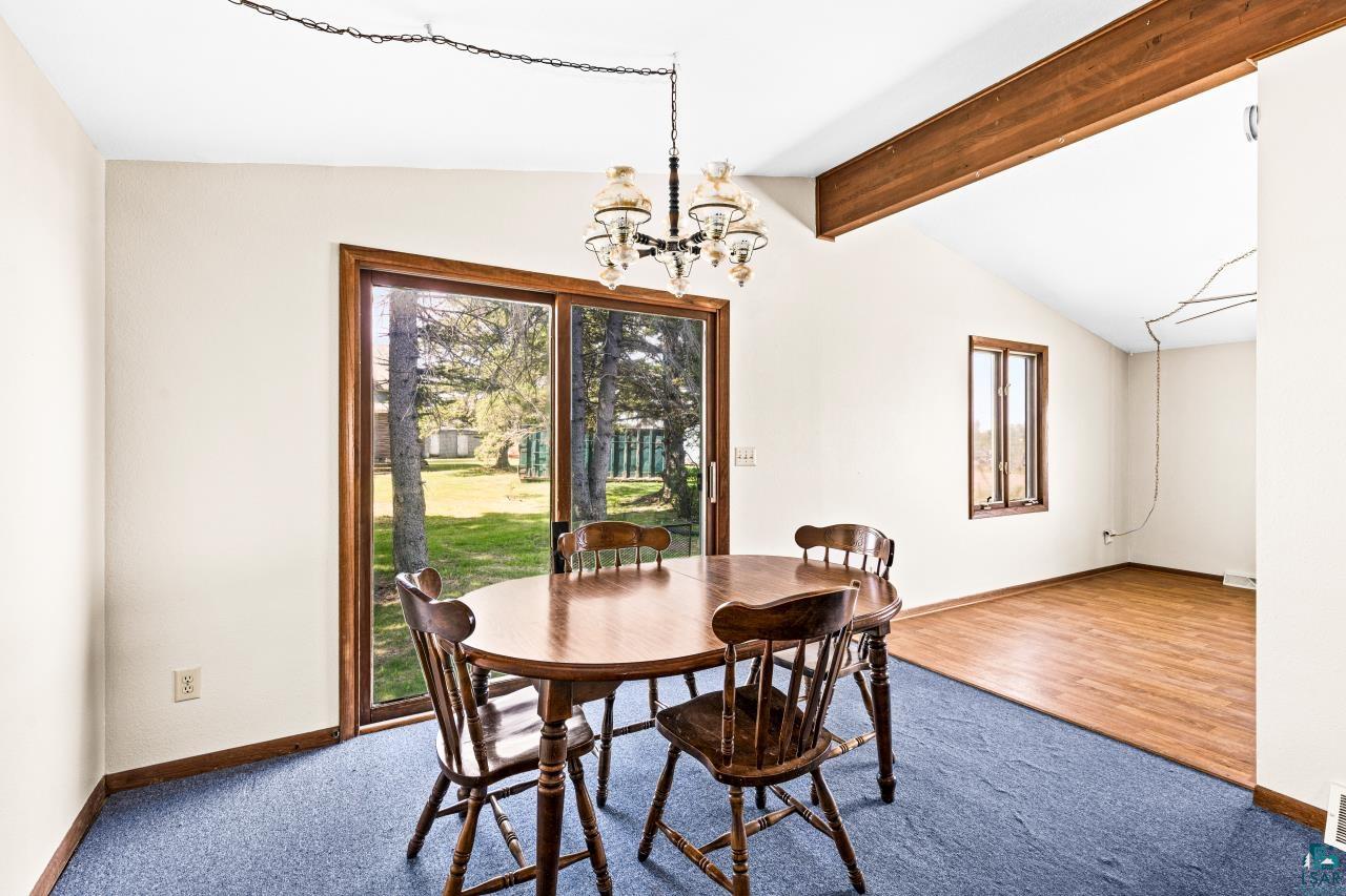 6606 Metso Road Kettle River, MN 55757 - Photo 13 of 84 Room featuring sliding glass door access to the exterior, vaulted ceiling with exposed wood beam, wood-frame window, and a mix of blue carpet and wood-finish flooring
