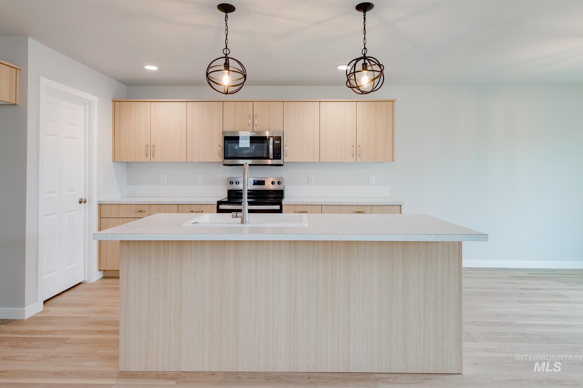 2391 West Fallon Loop Nampa, ID 83651 - Photo 2 of 20 Open-concept kitchen featuring an oversized island with an integrated sink, light wood-finish cabinetry, stainless steel appliances, and two spherical pendant light fixtures