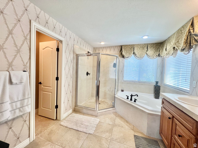 369 Culross Circle Tooele, UT 84074 - Photo 24 of 54 Spacious bathroom featuring a corner soaking tub, glass-enclosed shower, wood vanity with integrated sink, tiled flooring, and multiple windows with blinds