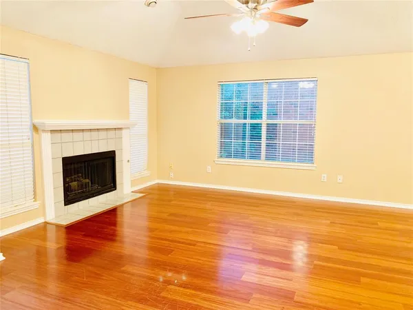 an empty room with wooden floor fireplace and windows