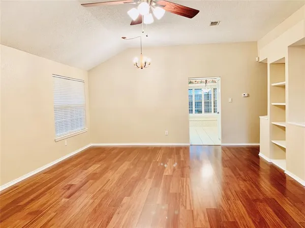 an empty room with wooden floor chandelier fan and windows