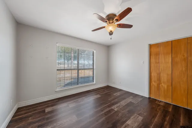 an empty room with wooden floor fan and windows