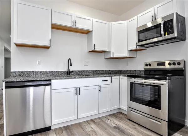 a kitchen with stainless steel appliances granite countertop white cabinets a sink and dishwasher a stove with wooden floor