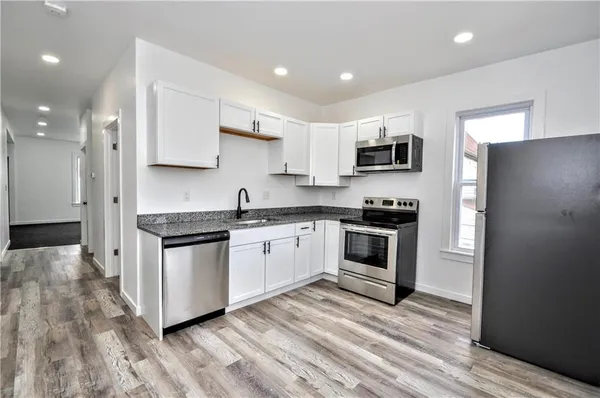 a kitchen with stainless steel appliances white cabinets a sink a stove a microwave and a refrigerator
