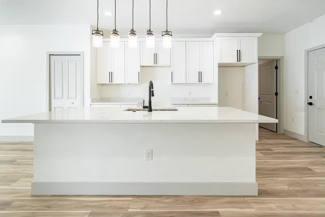 a large white kitchen with granite countertop a stove a sink a refrigerator and white cabinets with wooden floor