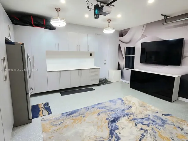 a large room with a large bed a flat tv screen and a view of kitchen