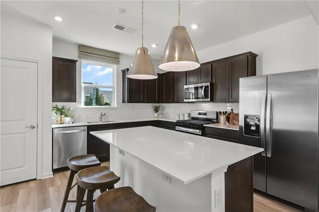 a kitchen with stainless steel appliances a sink a stove a refrigerator and chairs