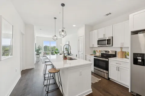 a kitchen with stainless steel appliances kitchen island granite countertop a stove a sink a refrigerator a dining table and chairs with wooden floor