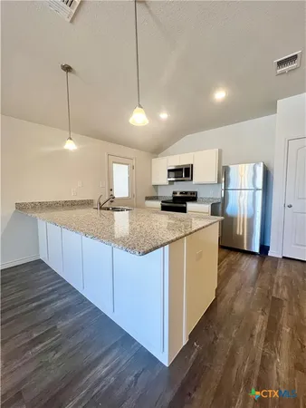 a large kitchen with stainless steel appliances granite countertop a stove a sink dishwasher a refrigerator white cabinets wooden floor and a fireplace